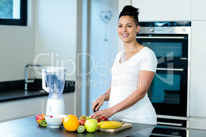 Portrait of pregnant woman cutting fruits on chopping board