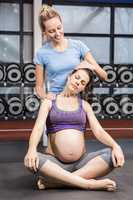 Smiling trainer helping pregnant woman stretching her neck