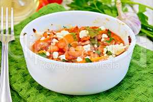 Shrimp and tomatoes with feta in white bowl on board