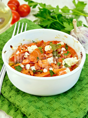 Shrimp and tomatoes with feta in white bowl on green napkin