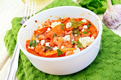 Shrimp and tomatoes with feta in white bowl on light board