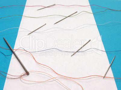 One large needle and several small needles for sewing, combined with colored threads across the sheet of paper