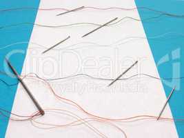 One large needle and several small needles for sewing, combined with colored threads across the sheet of paper