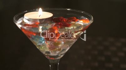 Candle burns in a glass with scattered gemstones