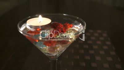 Candle burns in a glass with scattered gemstones
