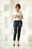 Businesswoman standing against white wall while looking at tablet
