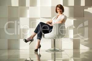 Elegant adult woman sitting in chair against of white modern wall