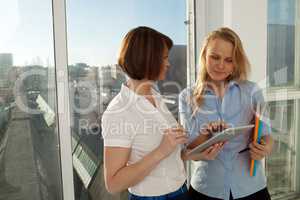 Two businesswomen standing against of city view from window.
