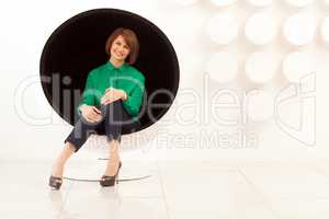 Attractive woman sitting on spherical chair with hands on knees