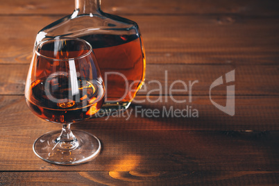 Glasses of cognac and bottle on the wooden table.