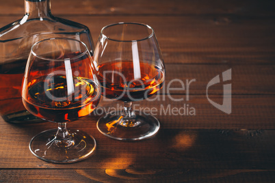 Two glasses of cognac and bottle on the wooden table.