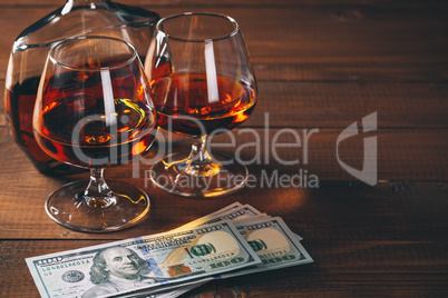 Two glasses of cognac and bottle, with wad of money on the wooden table.