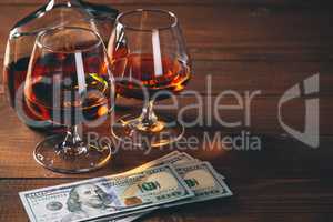 Two glasses of cognac and bottle, with wad of money on the wooden table.