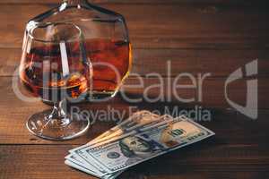Glass with cognac and bottle, with wad of money on the wooden table.