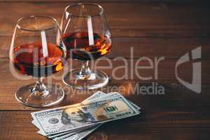 Two glasses of cognac with wad of money on the wooden table.