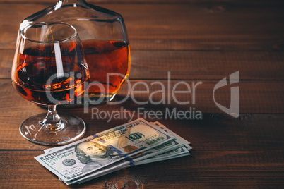Glass with cognac and bottle, with wad of money on the wooden table.