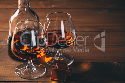 Two glasses of cognac and bottle on the wooden table.