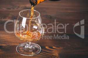 Pouring cognac or whiskey from the bottle into the glass against wooden background