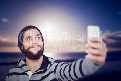 Composite image of hipster making face while taking selfie on mo
