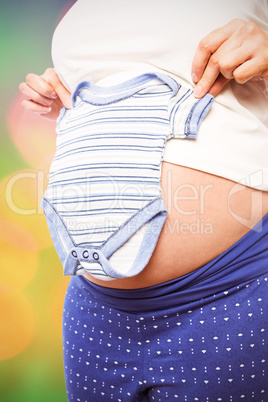 Composite image of pregnant woman holding baby clothes