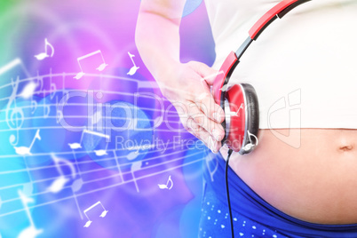 Composite image of pregnant woman holding earphones over bump