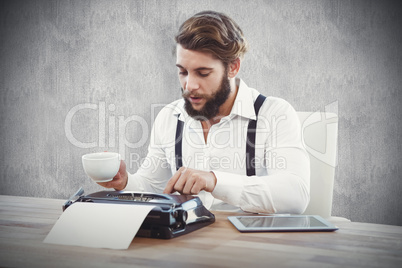 Composite image of hipster holding coffee working on typewriter