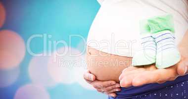 Composite image of pregnant woman holding baby shoes
