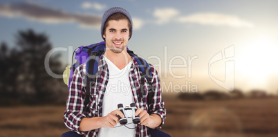 Composite image of happy hipster wearing backpack holding binocu