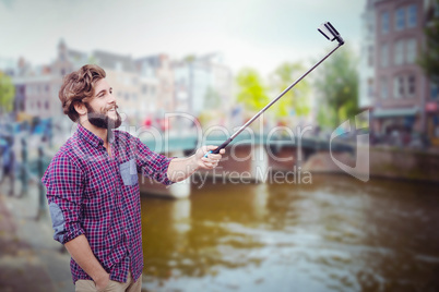 Composite image of happy hipster using selfie stick