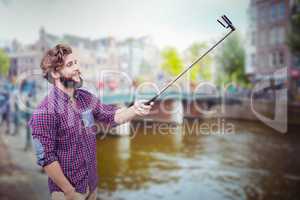 Composite image of happy hipster using selfie stick