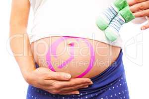 Composite image of pregnant woman holding baby shoes over bump