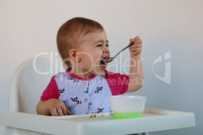 little girl eats porridge sits on a chair