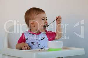 little girl eats porridge sits on a chair