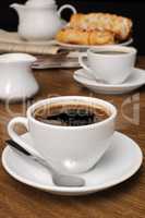 cup of fragrant black coffee on the table with milk and a bun
