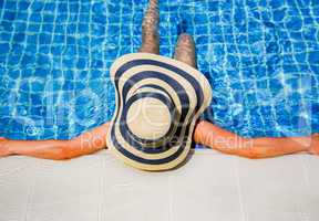 Woman in straw hat relaxing swimming pool