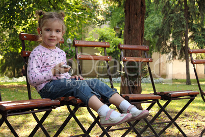 little girl sitting in the  park and listen music on phone