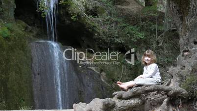 little girl sitting next to a waterfall