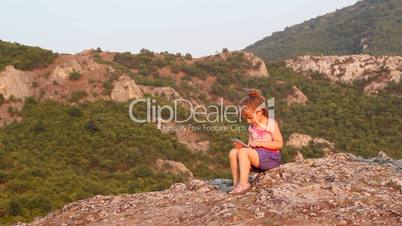 little girl sitting on a mountain top and play with tablet