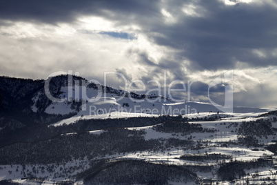 Village in winter mountains and storm clouds at evening