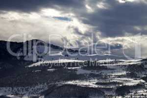 Village in winter mountains and storm clouds at evening