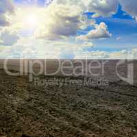 plowed field and sun on cloudy sky