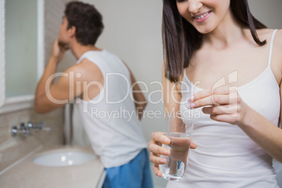 Beautiful woman putting pill in to a glass of water