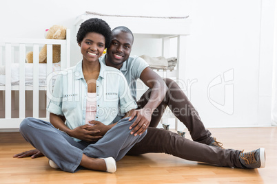 Pregnant couple sitting near baby cradle