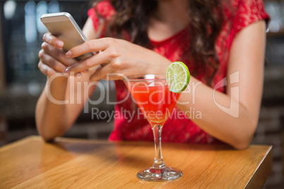 Pretty woman using her smartphone and having a cocktail