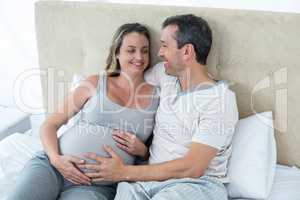 Expecting couple lying on bed and chatting