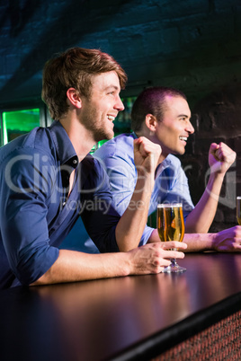 Two happy men raising their fist while having beer at bar counte