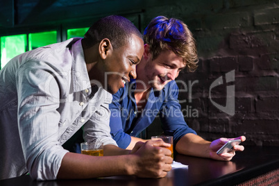 Two men looking at mobile phone and smiling at bar counter