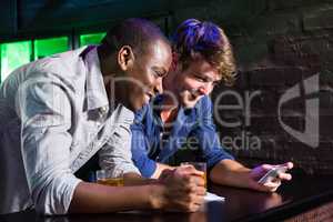 Two men looking at mobile phone and smiling at bar counter