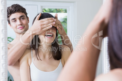 Man covering womans eyes while standing in front of bathroom mir