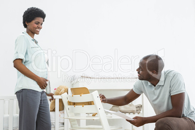 Pregnant woman looking at man fixing a baby chair